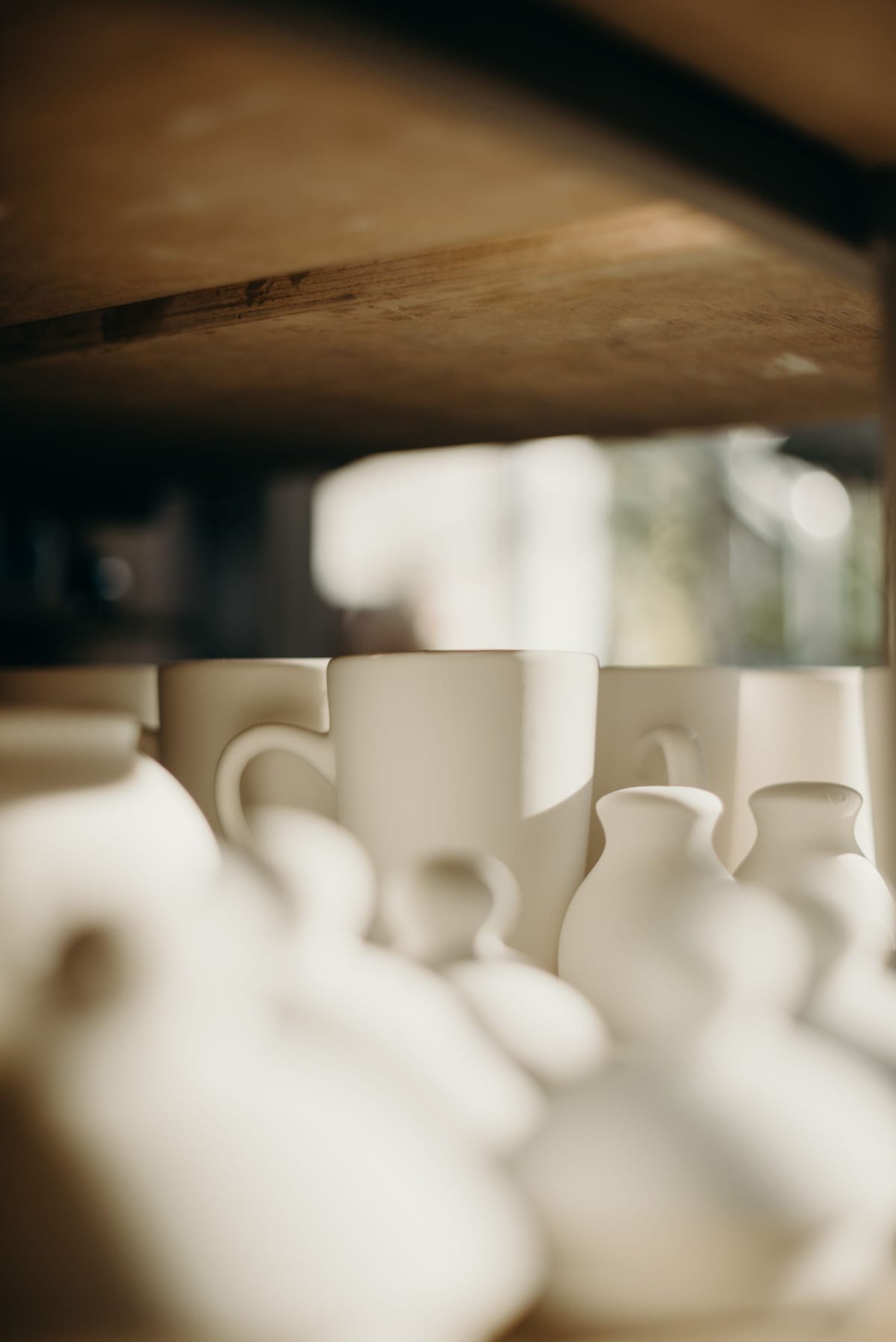 Small white ceramic vessels in shallow focus on a dark wooden shelf.