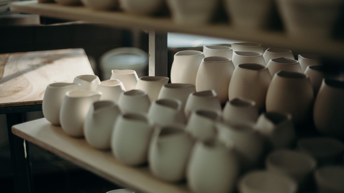 Groups of white pots and mugs catching directional light on a wooden shelf.