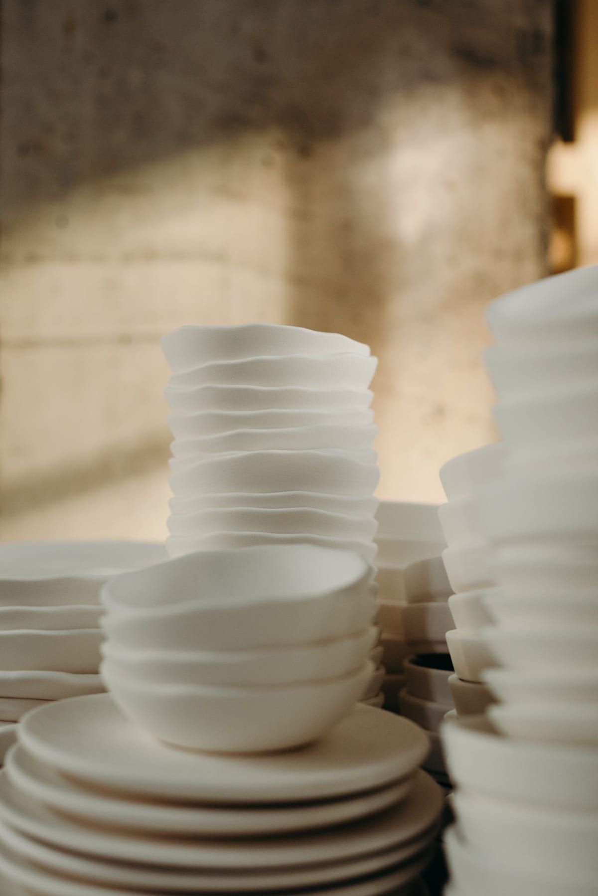 Stacks of pale ceramic bowls beside a textured workshop wall.