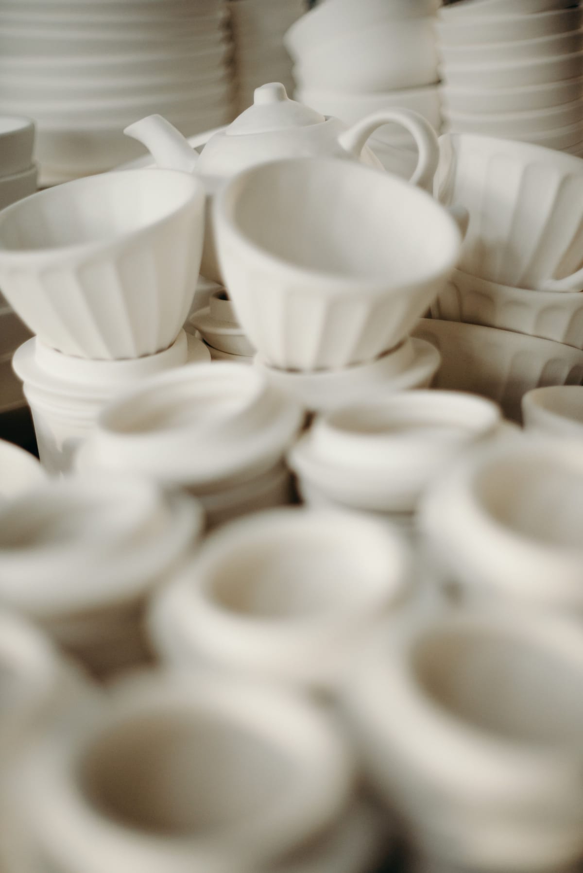 White ceramic cups and bowls arranged closely together in soft focus.