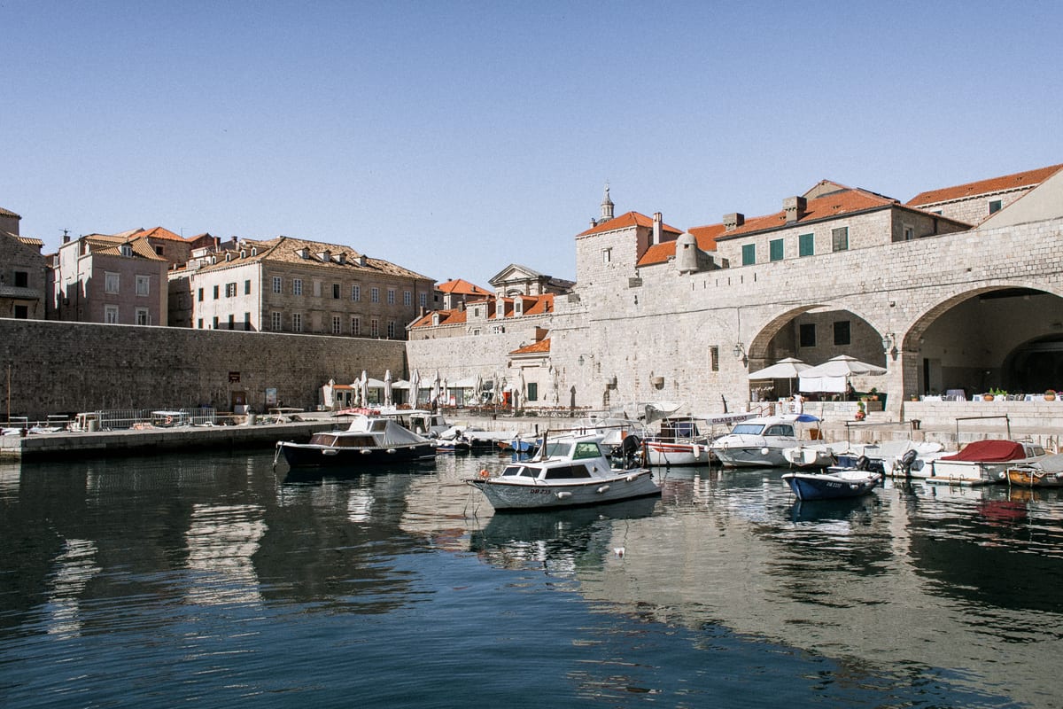 Boats in Dubrovnik's old port, with pale historic buildings behind them.