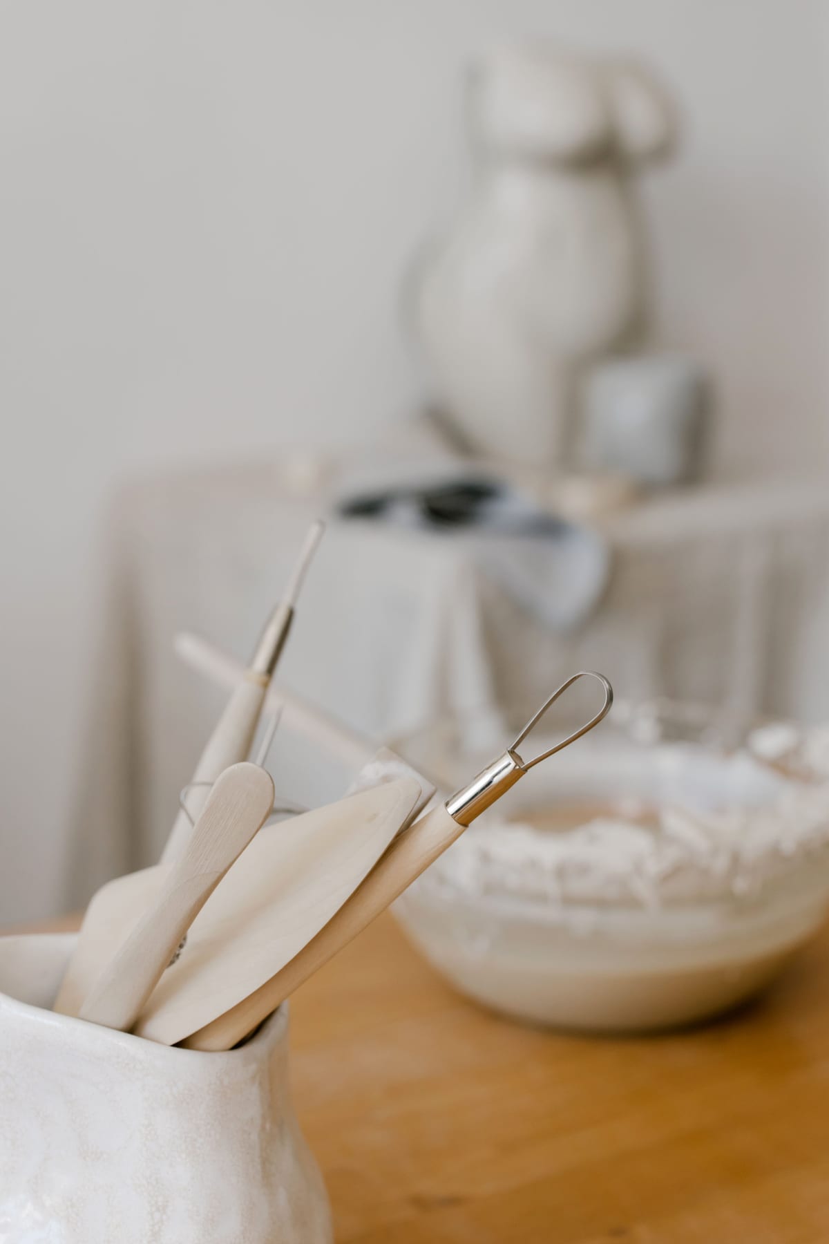 Wooden pottery tools in a ceramic holder with a small sculpture behind them.