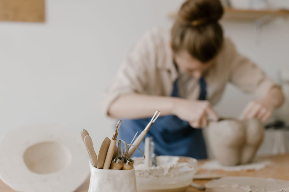 Wooden sculpting tools in the foreground with a potter working at the same table.