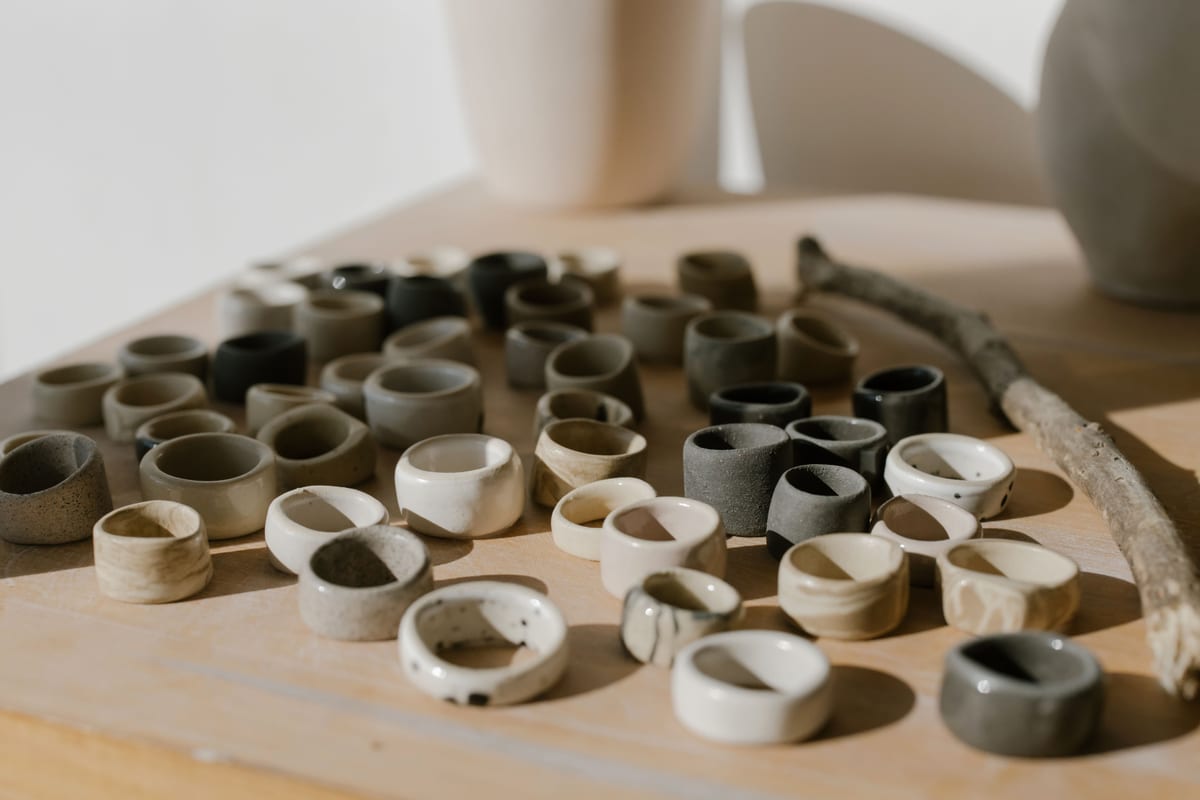 A group of handmade ceramic rings in pale tones arranged on a wooden surface.