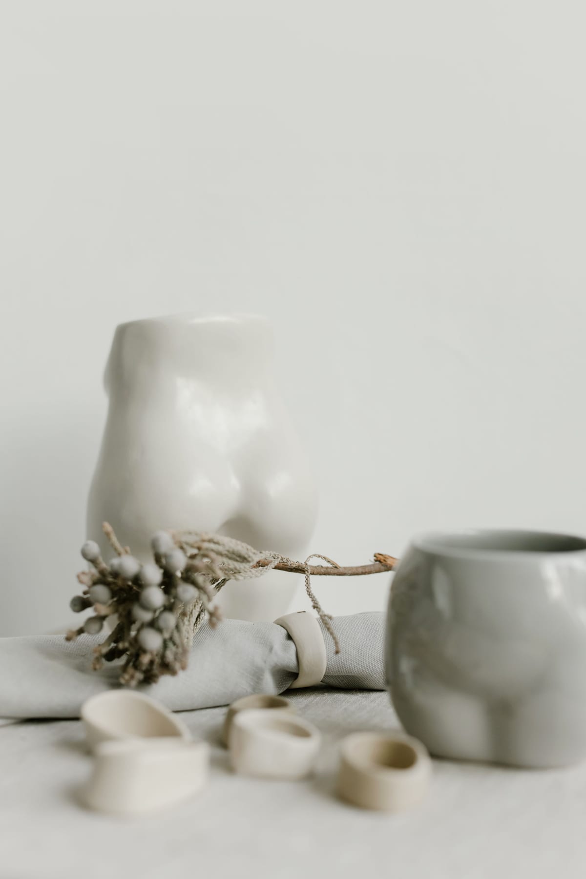 A close view of softly lit white vessels and ceramic rings on fabric.